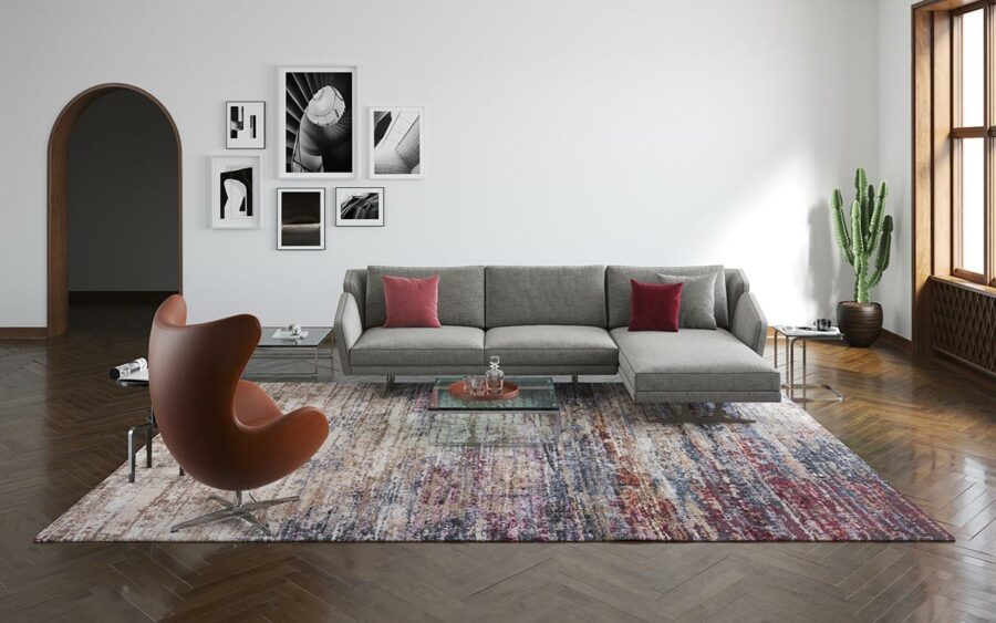 Modern eingerichtetes Wohnzimmer mit grauem Ecksofa, buntem Teppich, braunem Designer-Sessel, Wandbildern in Schwarz-Weiß, Holzboden und einem Fenster auf der rechten Seite.