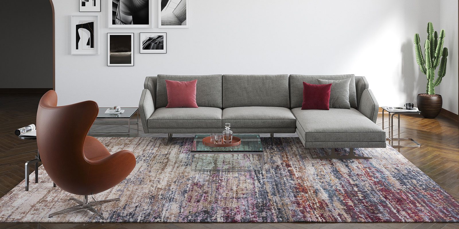 Modernes Wohnzimmer mit grauer L-förmiger Couch mit roten Kissen, braunem Ei-Sessel, gemustertem Teppich, Glastisch und Dekopflanze. Helle Wände mit Schwarz-Weiß-Fotografien. Dunkler Holzboden.
