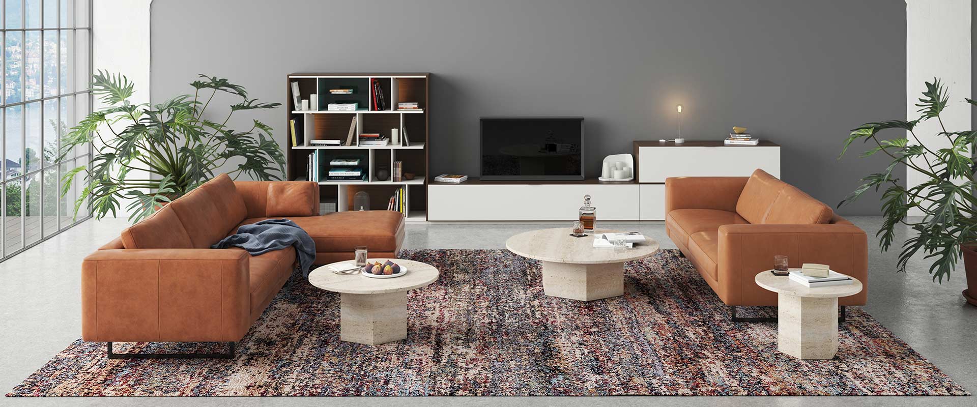 Modernes Wohnzimmer mit großem Fenster, zwei cognacfarbenen Ledersofas, zwei runden Marmortischen und einem Bücherregal. Dekorative Pflanzen und ein gemusterter Teppich ergänzen den Raum.