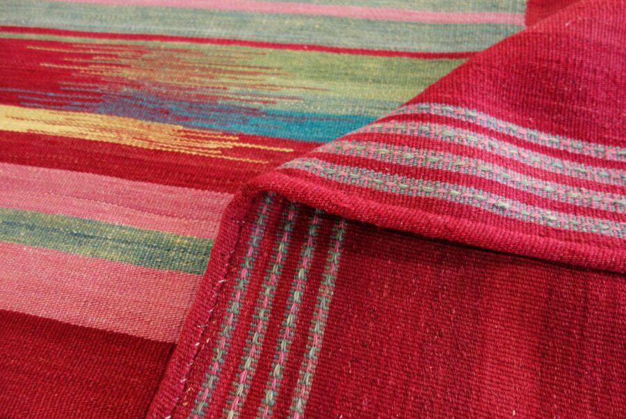 Texturierte rote Teppiche mit vielfarbigen Streifenmustern und Details in Grün, Blau, Gelb und Weiß, teilweise aufgefaltet.