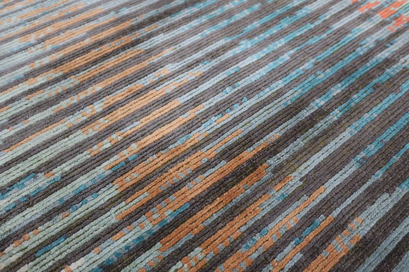 Nahaufnahme eines gemusterten Teppichs mit horizontalen Streifen in Grau-, Blau-, Türkis- und Brauntönen.