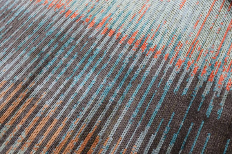 Nahaufnahme eines gemusterten Teppichs mit horizontalen Streifen in Grau-, Blau-, Türkis- und Brauntönen.