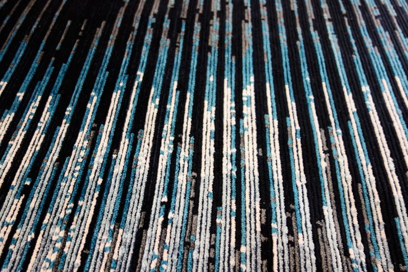 Nahaufnahme eines strukturierten Teppichs mit einem Muster aus parallelen Linien in Schwarz, Weiß und verschiedenen Blautönen.