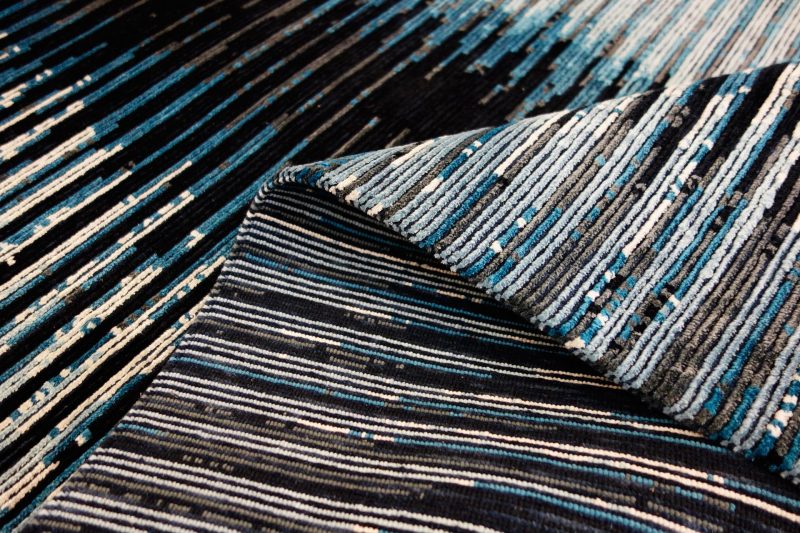 Nahaufnahme eines strukturierten Teppichs mit einem Muster aus parallelen Linien in Schwarz, Weiß und verschiedenen Blautönen.