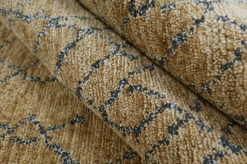 Nahaufnahme eines gemusterten Teppichs mit beige-brauner Textur und dunklen Akzenten in organischem Design.