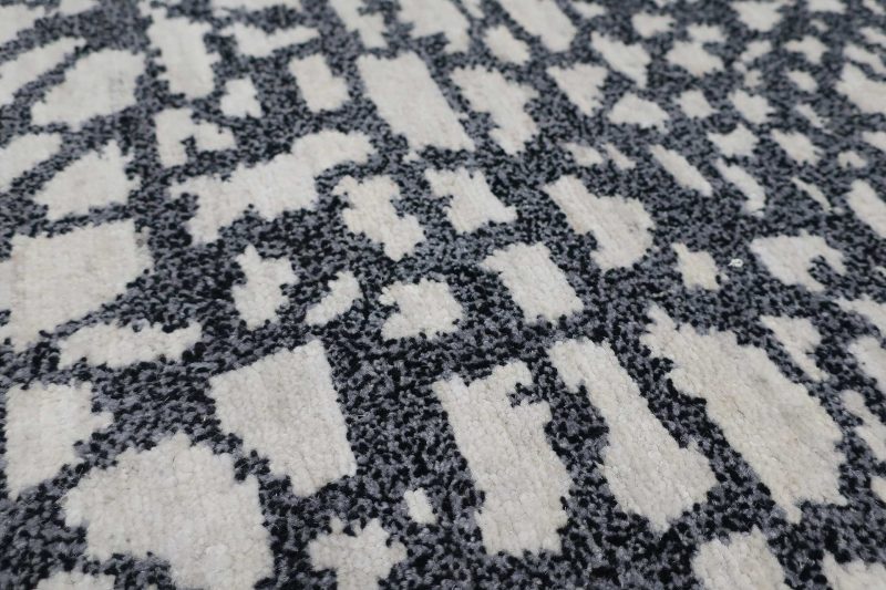 Nahaufnahme eines gemusterten Teppichs mit unregelmäßigen schwarzen und weißen Formen auf grauem Hintergrund.