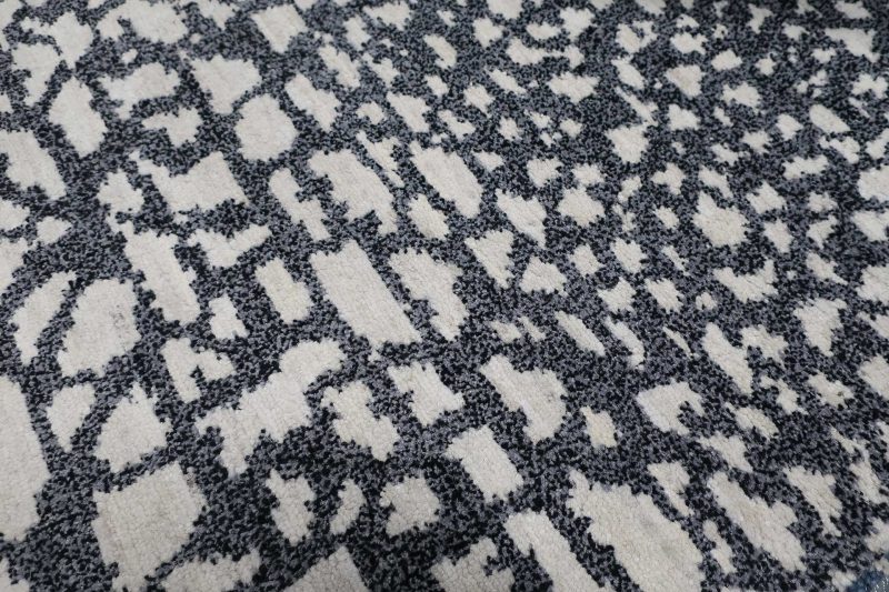 Nahaufnahme eines gemusterten Teppichs mit unregelmäßigen schwarzen und weißen Formen auf grauem Hintergrund.