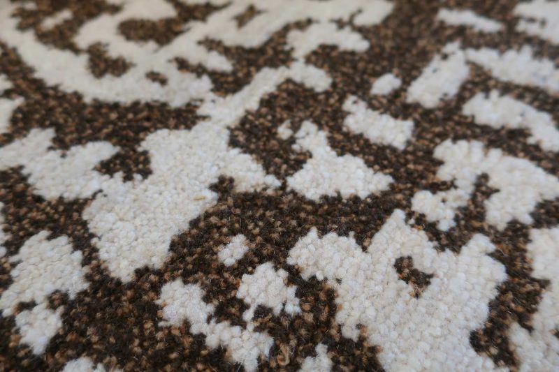 Nahaufnahme eines gemusterten Teppichs mit unregelmäßigen dunkelbraunen und weißen Formen.