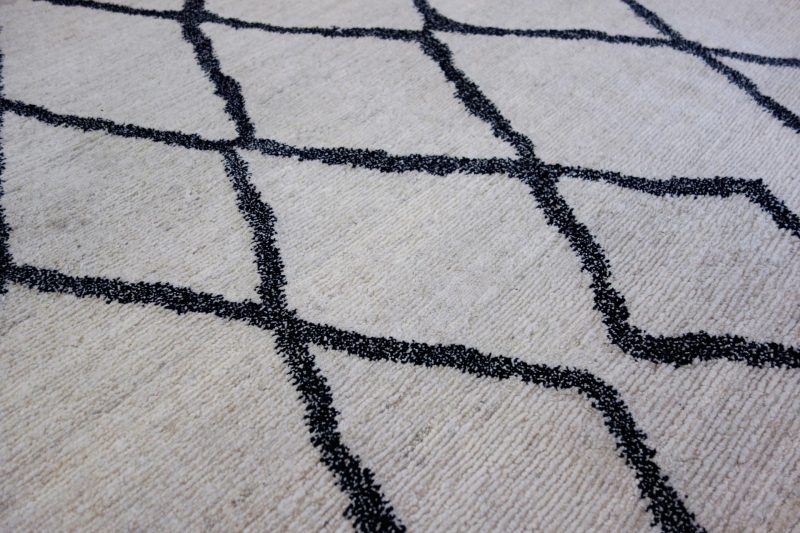 Detailaufnahme eines flauschigen Teppichs mit einem geometrischen Muster aus schwarzen Linien auf einem cremefarbenen Hintergrund.
