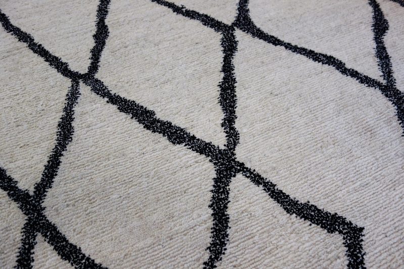 Detailaufnahme eines flauschigen Teppichs mit einem geometrischen Muster aus schwarzen Linien auf einem cremefarbenen Hintergrund.