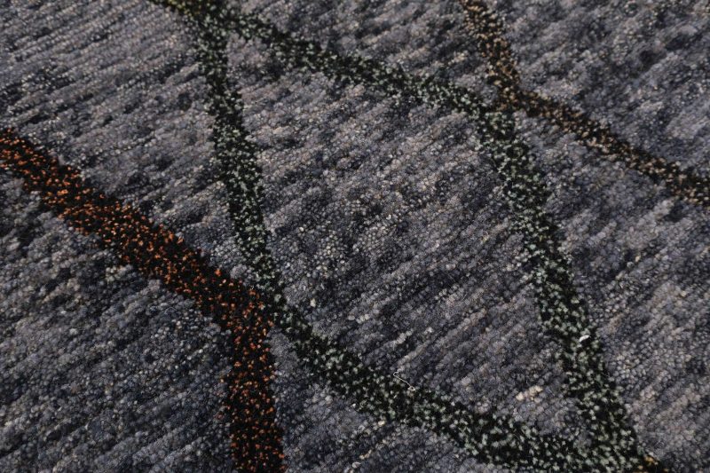 Nahaufnahme eines strukturierten Teppichs mit geometrischen Mustern in Grau-, Schwarz- und Rosttönen.