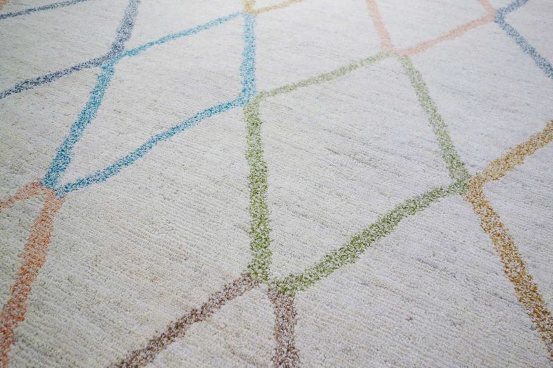 Nahaufnahme eines texturierten Teppichs mit einem abstrakten Muster aus mehrfarbigen Linien in Blau, Grün und Orange.