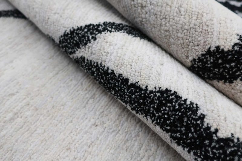 Nahaufnahme eines Teppichs mit einem abstrakten Muster aus dicken schwarzen Linien auf einem hellbeigen Hintergrund.