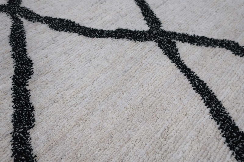 Nahaufnahme eines Teppichs mit einem abstrakten Muster aus dicken schwarzen Linien auf einem hellbeigen Hintergrund.