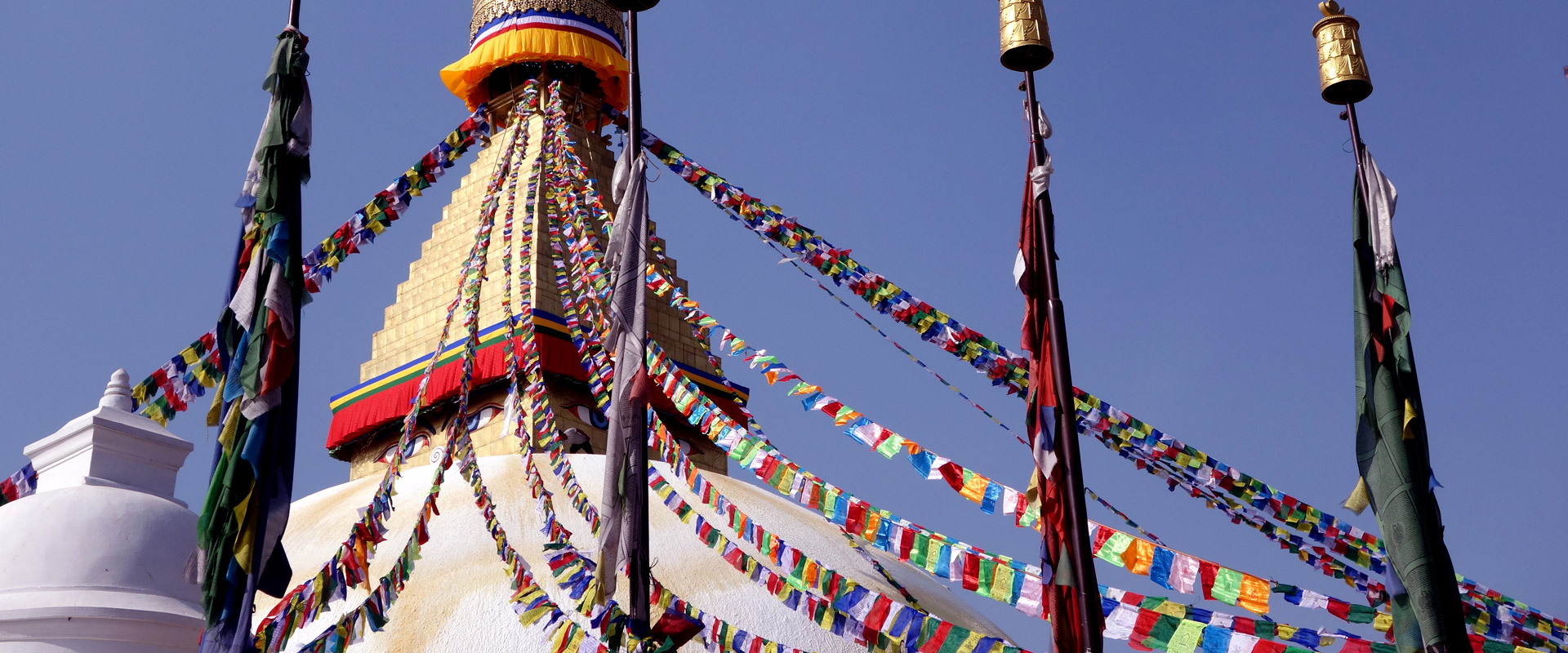 Bunte Gebetsfahnen, die von einem Stupa mit goldener Spitze in den blauen Himmel strahlen, umgeben von klarer Luft und Sonnenschein.